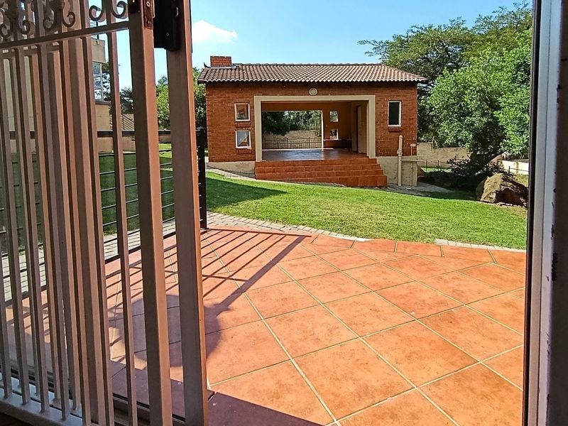 A view of a rear garden featuring a tiled patio area, a well-maintained lawn, and a detached brick outbuilding with a tiled roof.