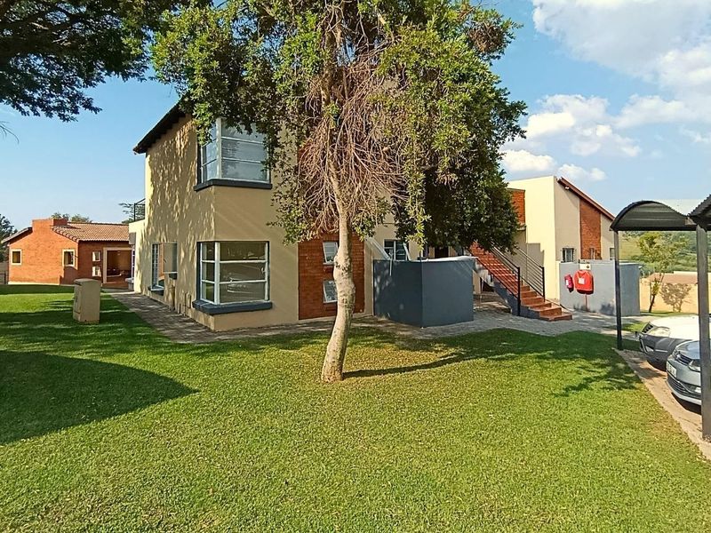 Exterior view of the apartment complex featuring a paved driveway, carport, landscaped lawn, and brick-accented building facade with an external staircase.
