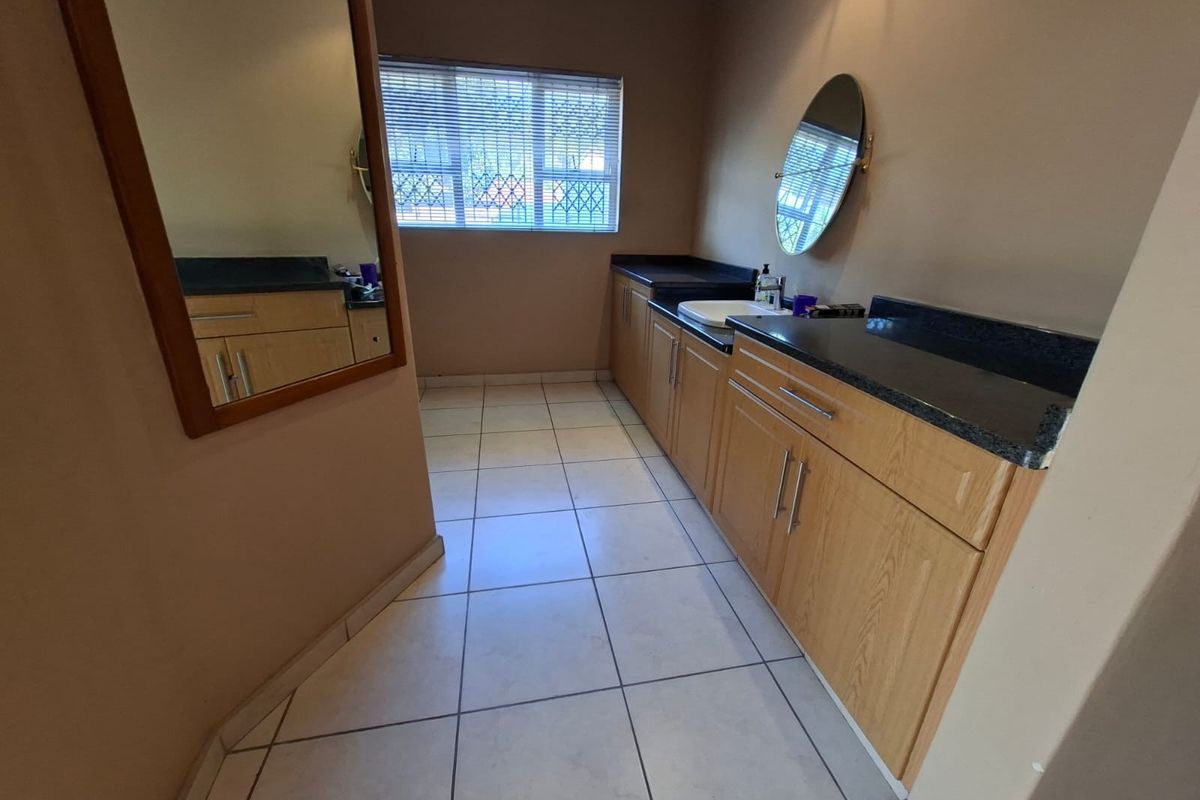 A functional bathroom vanity area featuring light wood cabinetry, dark granite countertops, a drop-in sink, and tiled flooring.