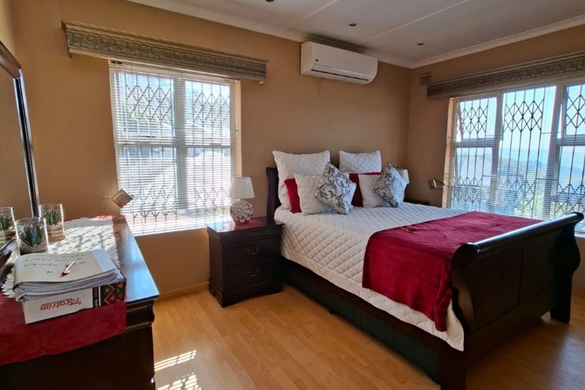 A well-maintained bedroom featuring laminate flooring, recessed ceiling lighting, and a wall-mounted air conditioning unit.
