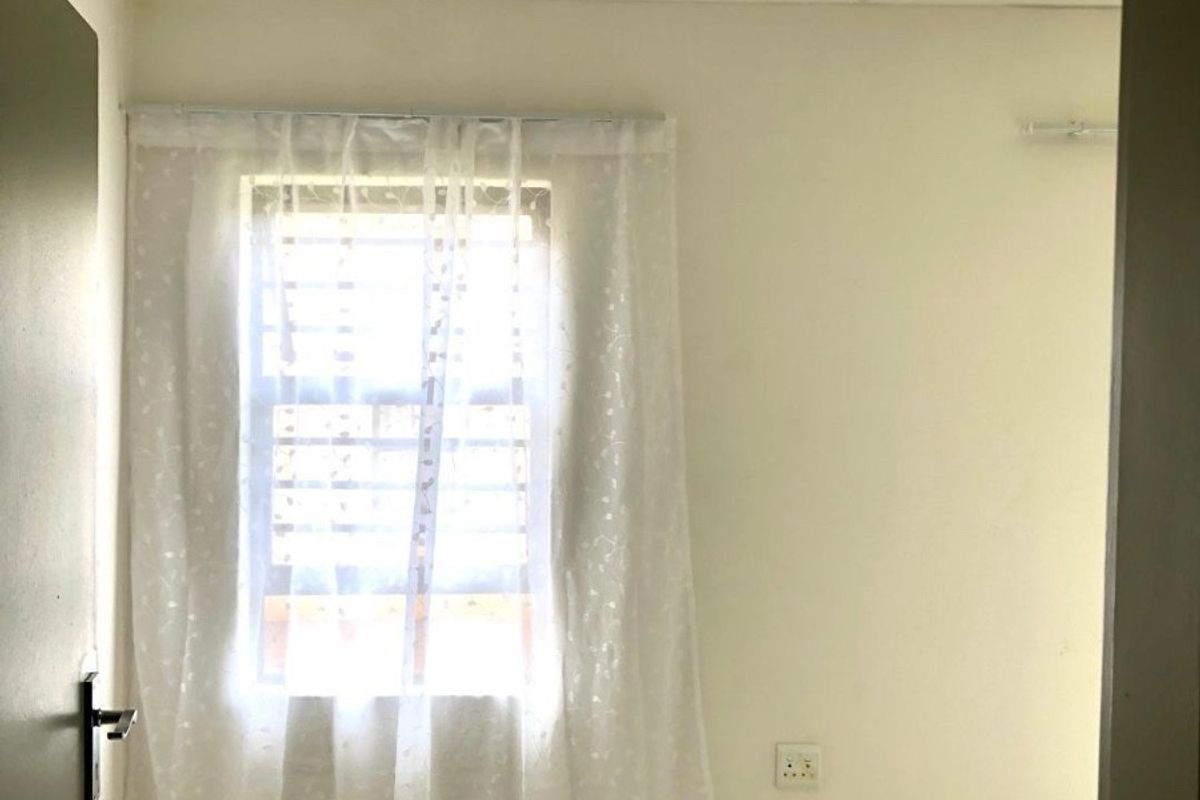 A bright, empty bedroom featuring tiled flooring, a ceiling light fixture, and a window fitted with security bars.