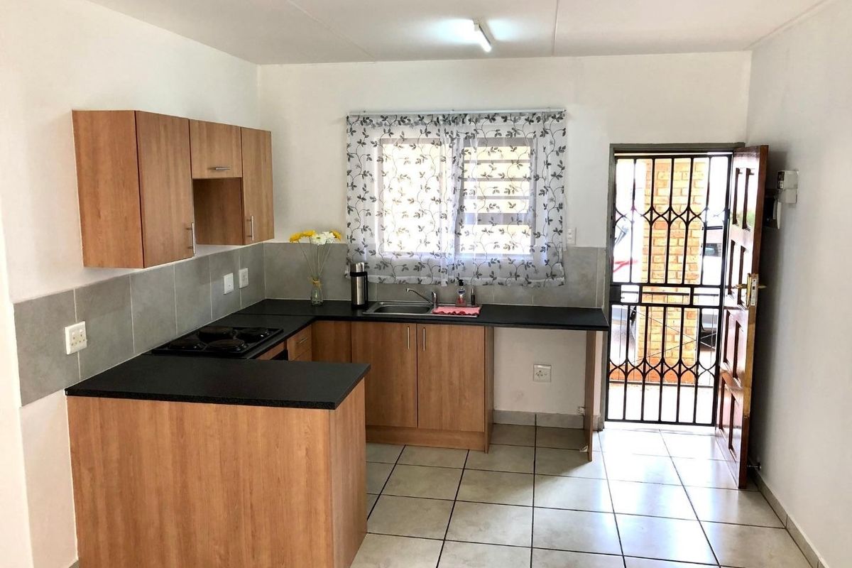 A functional kitchen featuring laminate cabinetry, black countertops, a built-in hob, and tiled flooring, with direct access to an exterior security gate.