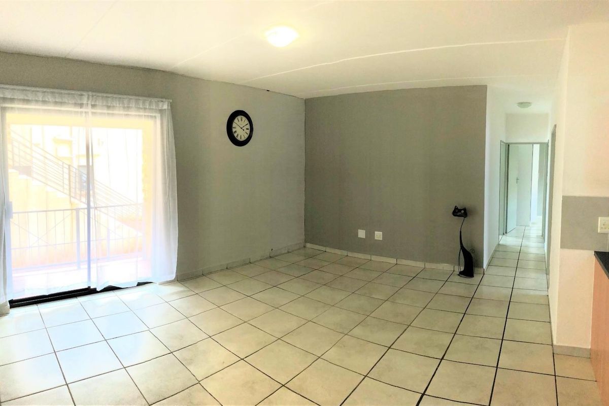 A bright, open-plan living area featuring neutral tiled flooring and a sliding glass door providing access to the exterior.