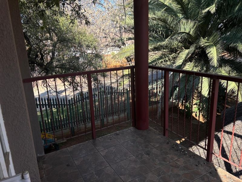 A covered balcony featuring tiled flooring and a metal railing, overlooking the garden and street area.
