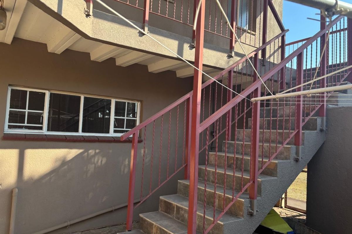 Exterior view of the rear property elevation featuring a concrete staircase with metal railings leading to an upper level balcony.