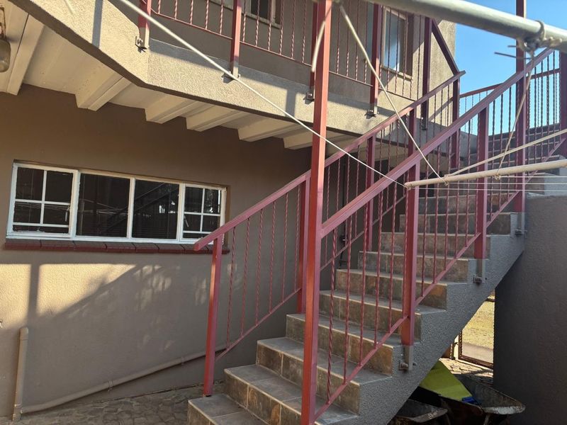 Exterior view of the rear property elevation featuring a concrete staircase with metal railings leading to an upper level balcony.