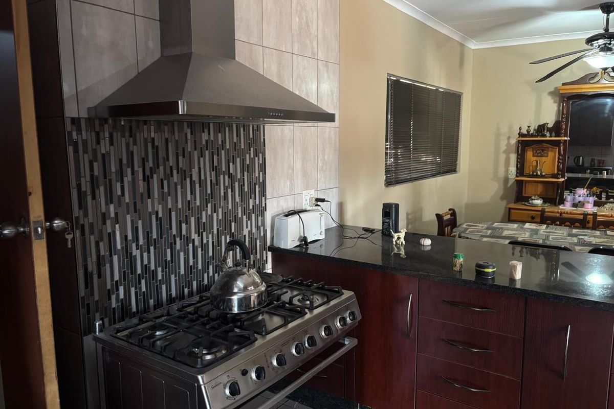 A functional kitchen featuring dark wood cabinetry, granite countertops, a stainless steel gas stove with extractor fan, and a decorative mosaic tile backsplash.