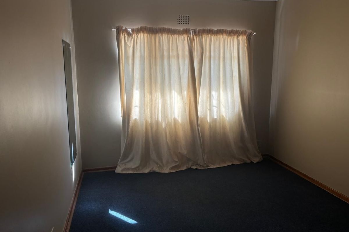 A simple, empty bedroom featuring dark carpeting, neutral wall tones, and a window with curtains, offering a blank canvas for personalization.