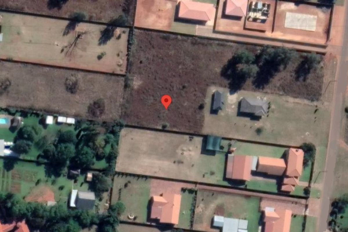 An aerial view of a vacant residential plot situated within a developed suburban neighborhood.