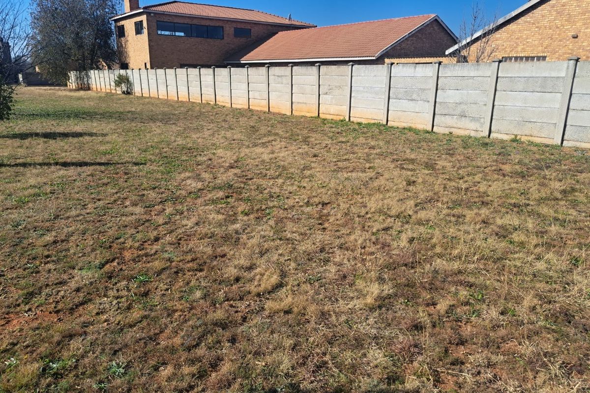 A view of a vacant residential plot featuring dry grass and a precast concrete boundary wall.