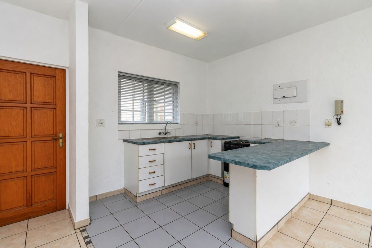 A functional kitchen featuring white cabinetry, a blue laminate countertop, tiled splashback, and a built-in stove, with neutral floor tiles throughout.