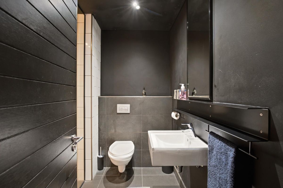 Modern bathroom featuring dark matte wall finishes, a wall-mounted toilet, and a sleek basin with chrome fixtures.