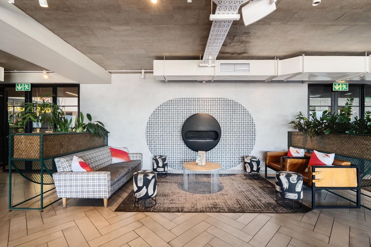 Modern living area featuring an exposed concrete ceiling, industrial HVAC ducting, a striking circular wall-mounted fireplace, and stylish herringbone tile flooring.