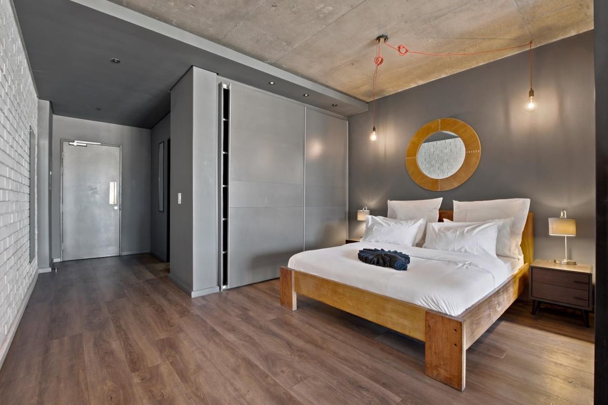 Modern bedroom featuring an exposed concrete ceiling, built-in wardrobe, and stylish painted brick wall with warm pendant lighting.