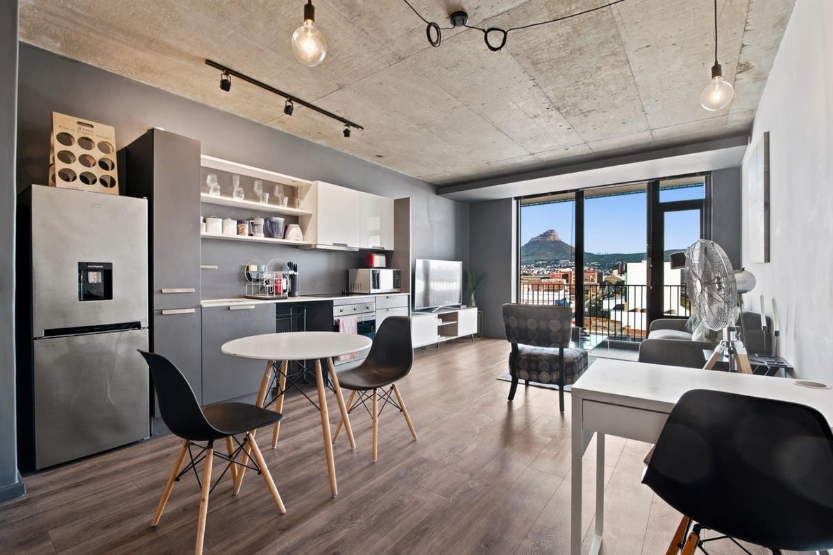 Modern open-plan apartment featuring an exposed concrete ceiling, laminate flooring, and a sleek kitchen, with direct access to a balcony offering scenic views.