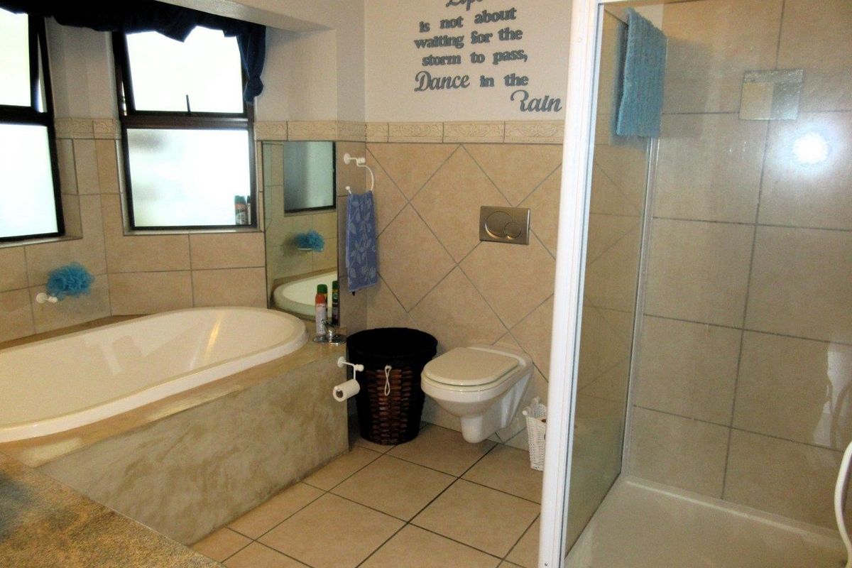 A functional bathroom featuring a built-in bathtub, a separate glass-enclosed shower, and a wall-mounted toilet with neutral tiled finishes.