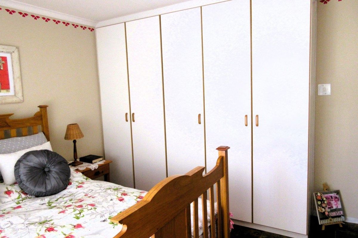 A bedroom featuring floor-to-ceiling built-in white wardrobes with simple hardware, providing ample storage space.