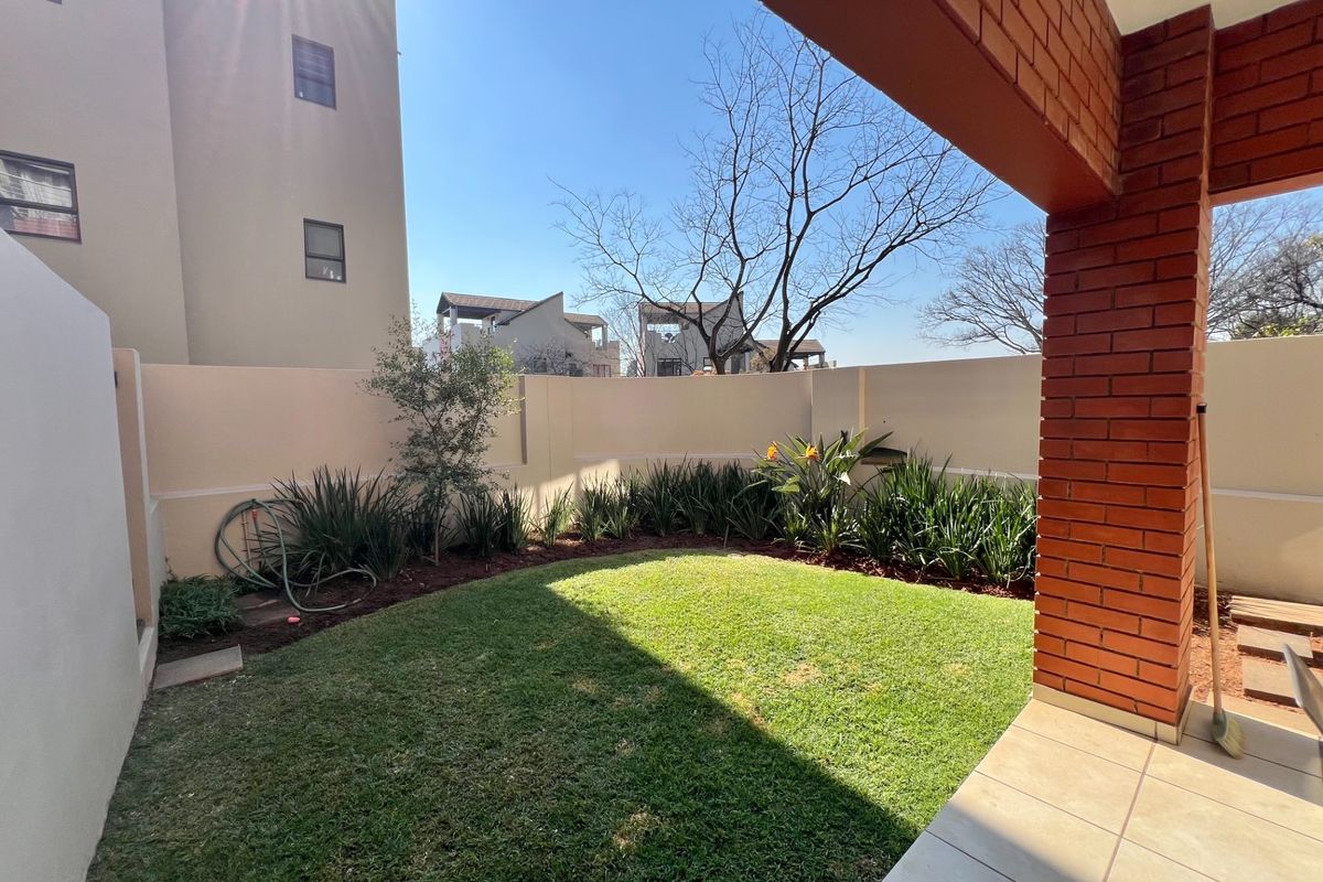 A private rear garden featuring a manicured lawn, perimeter boundary walls, and a covered patio area with exposed brick pillars.