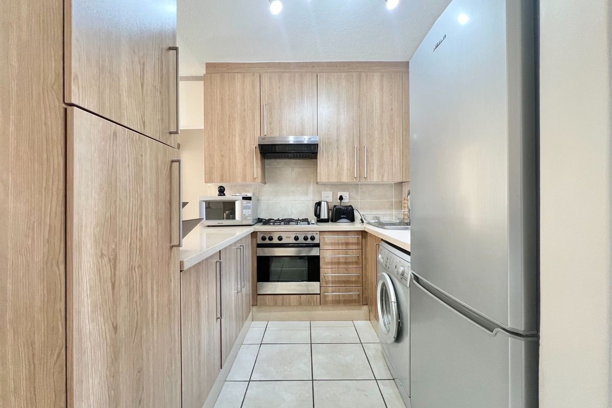 A compact, functional kitchen featuring light wood-grain cabinetry, tiled flooring, a built-in oven, gas hob, extractor fan, and integrated laundry plumbing.