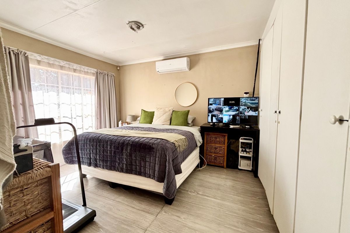 A functional bedroom featuring built-in wardrobes, a wall-mounted air conditioning unit, and large windows allowing for natural light.