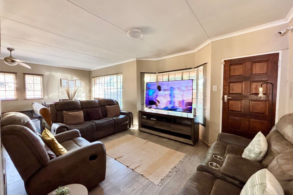 Spacious living room featuring wood-look flooring, large bay windows, and a classic timber entrance door, creating a comfortable and functional family living space.