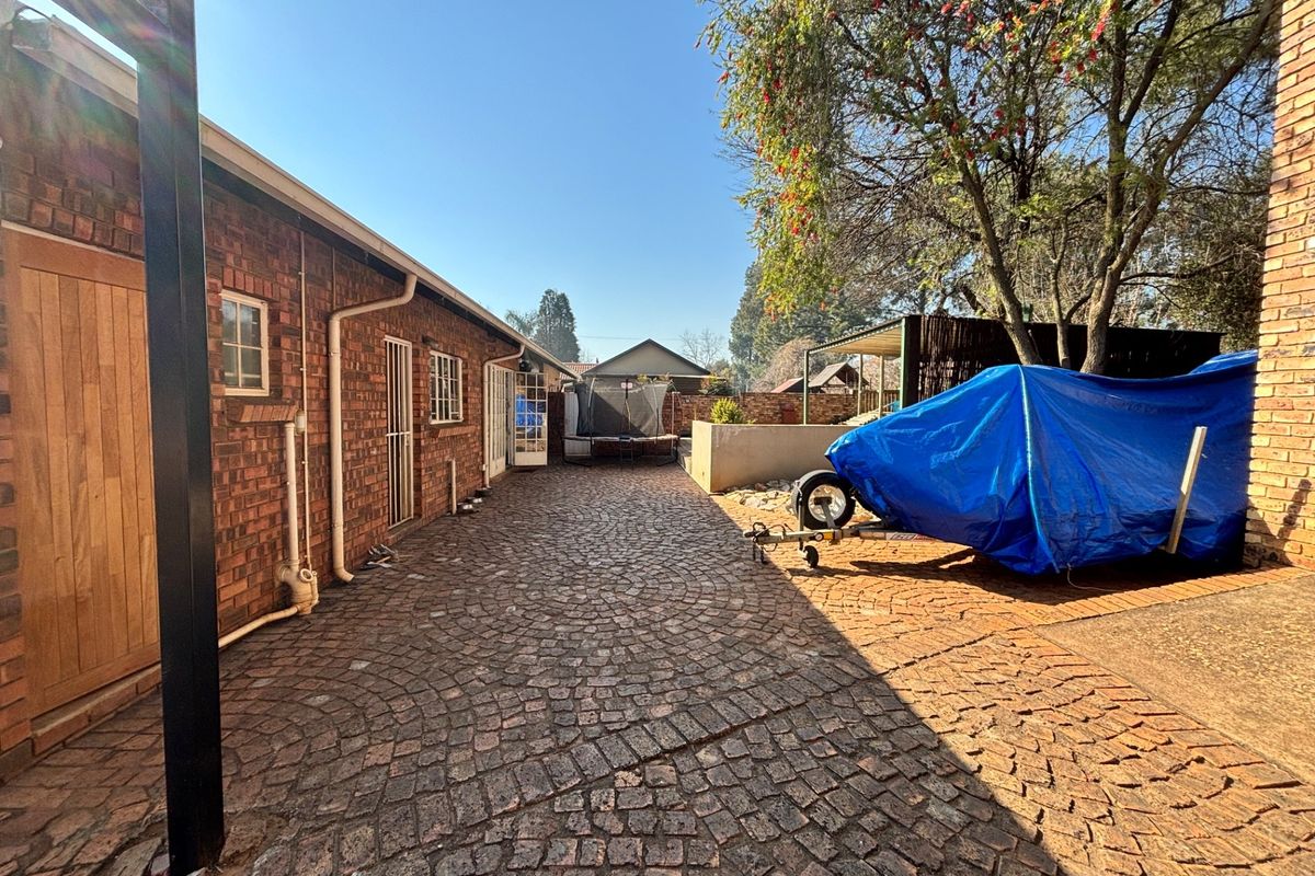 A paved rear exterior area featuring exposed brick walls, established trees, and access to the main dwelling.