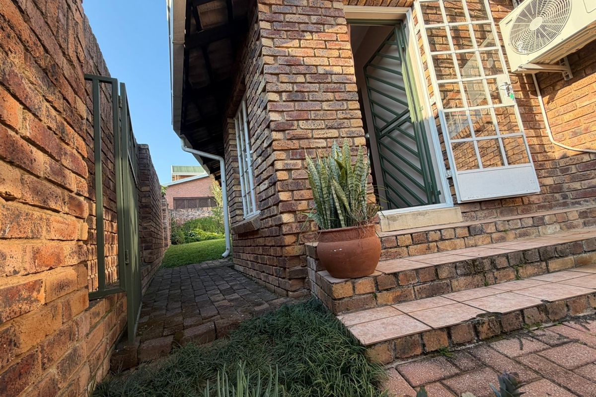 A side view of the property featuring face brick exterior, paved pathways, tiled entrance steps, and a mounted air conditioning unit.