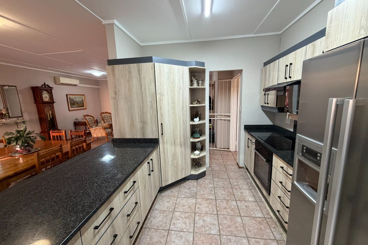Modern kitchen featuring light wood-grain cabinetry, dark granite countertops, integrated appliances, and tiled flooring, flowing into an adjacent dining area.