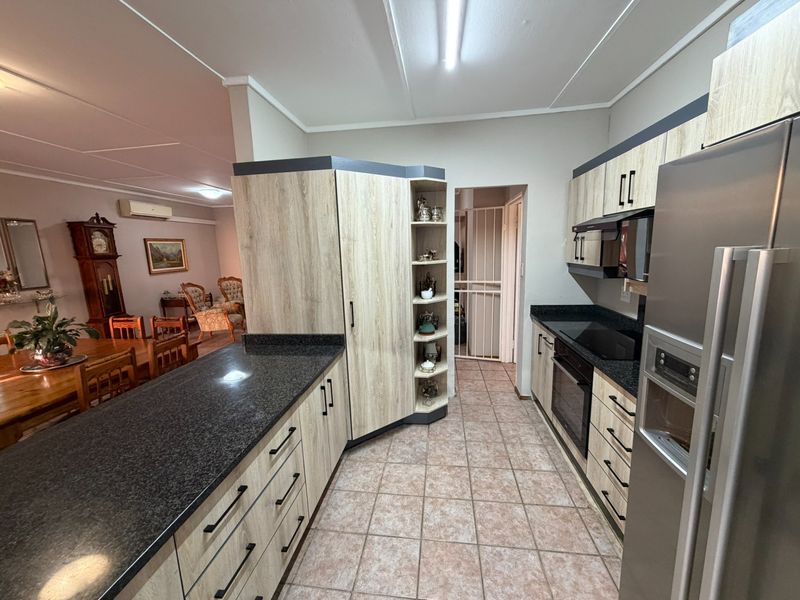 Modern kitchen featuring light wood-grain cabinetry, dark granite countertops, integrated appliances, and tiled flooring, flowing into an adjacent dining area.