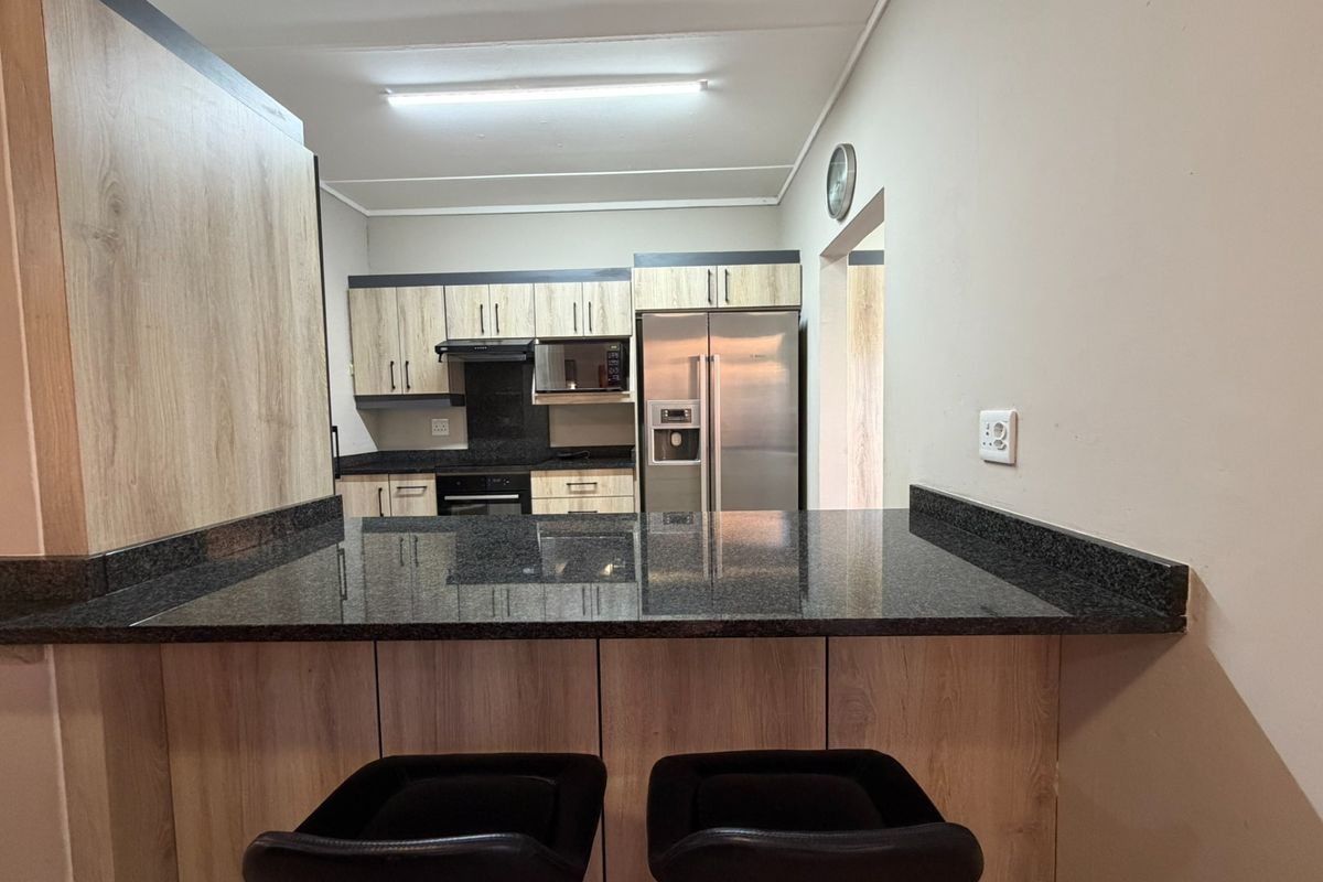 Modern kitchen featuring light wood-grain cabinetry, dark granite countertops, a breakfast bar, and integrated appliances.