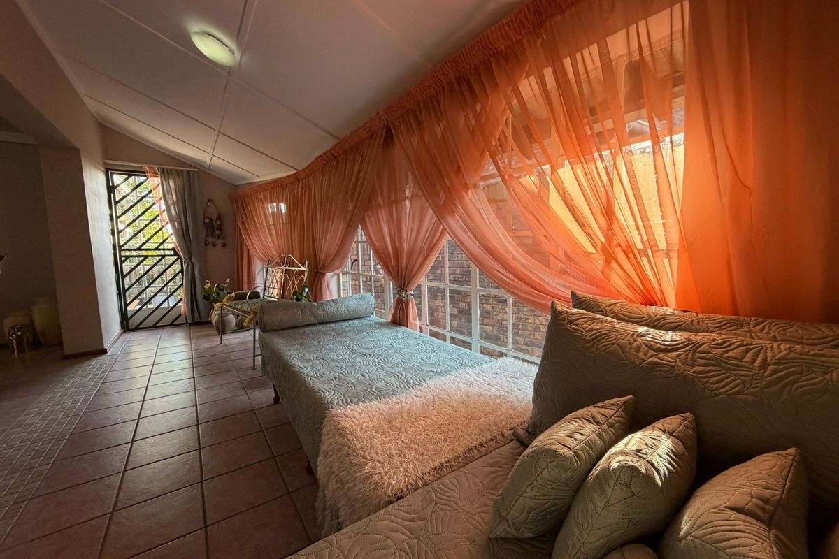 A sunlit living area featuring tiled flooring, large windows with draped curtains, and a secure metal entrance gate.