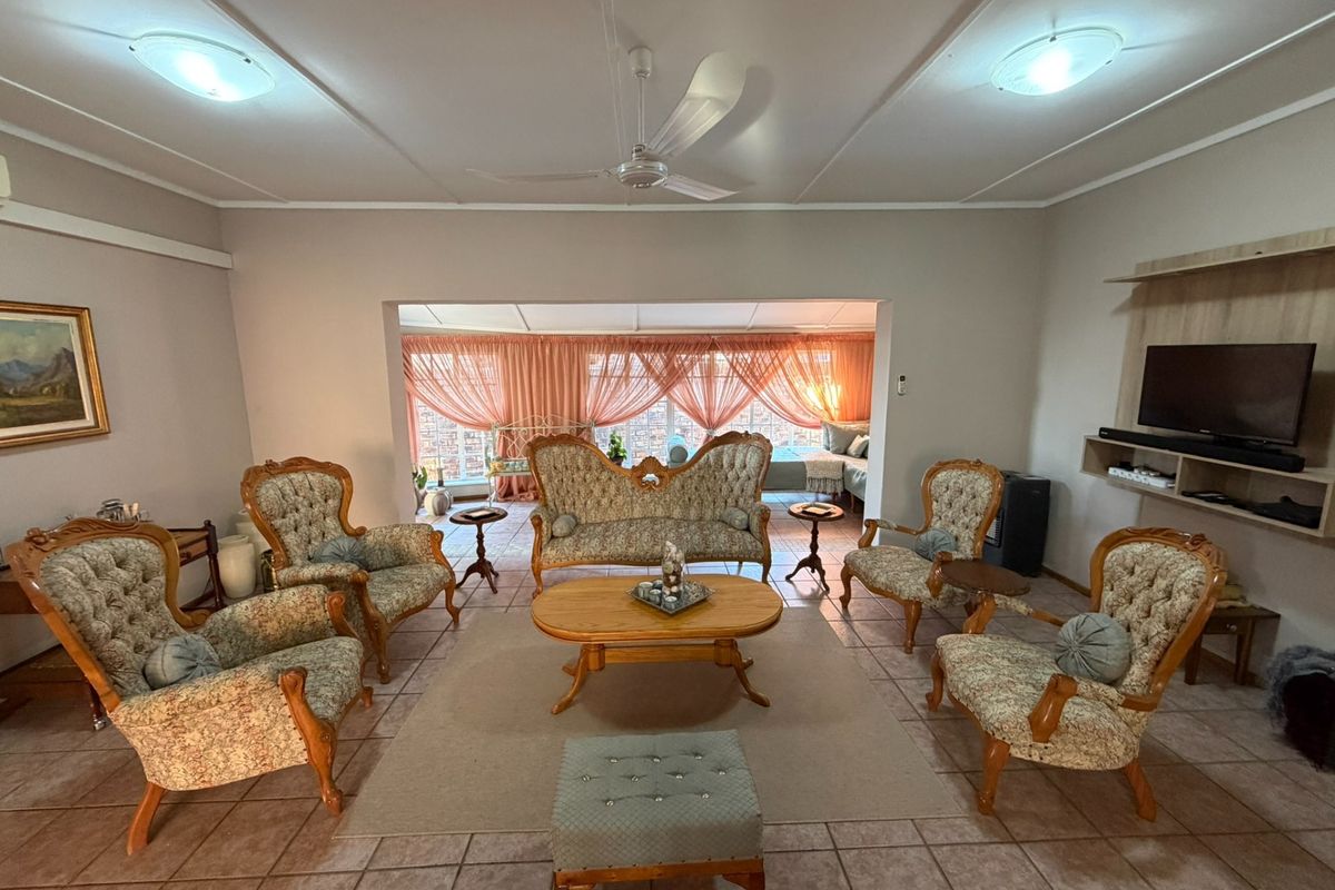 Spacious living room featuring tiled flooring, a ceiling fan, and built-in media shelving, with an open transition to an adjacent sunroom area.