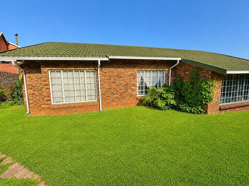 A view of the rear exterior of the house featuring a face brick facade, green tiled roof, and well-maintained lawn.