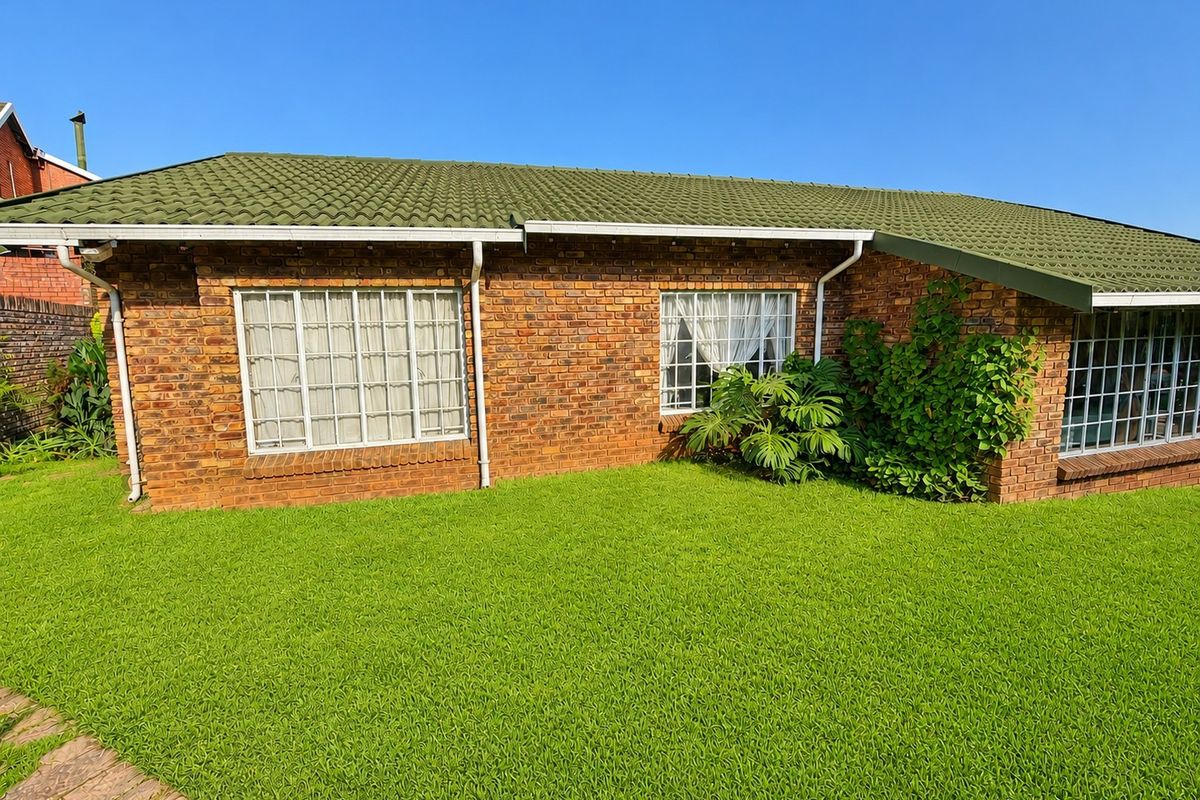 A view of the rear exterior of the house featuring a face brick facade, green tiled roof, and well-maintained lawn.