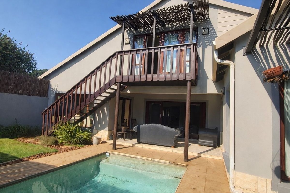 Rear exterior view featuring a swimming pool, tiled patio area, and an elevated timber balcony with external staircase access.