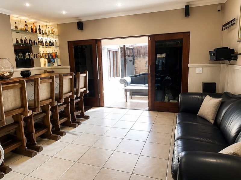 A dedicated bar area featuring a built-in counter, glass shelving, tiled flooring, and sliding doors providing direct access to an outdoor patio space.
