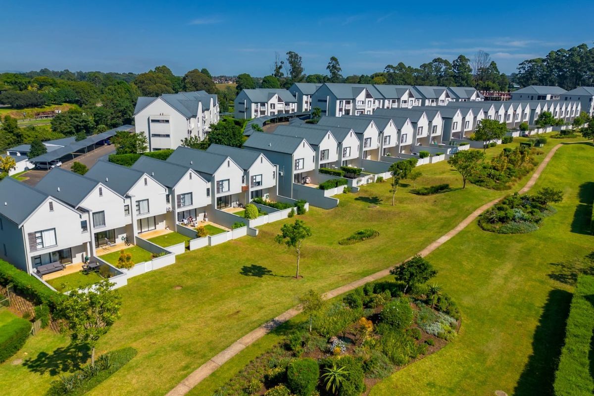 Aerial view of a modern townhouse complex featuring uniform architectural design, pitched roofs, private garden patios, and extensive landscaped communal green spaces.