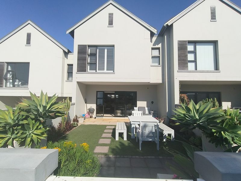 Rear view of a modern townhouse featuring a paved patio, artificial lawn, and sliding glass doors leading into the living area.