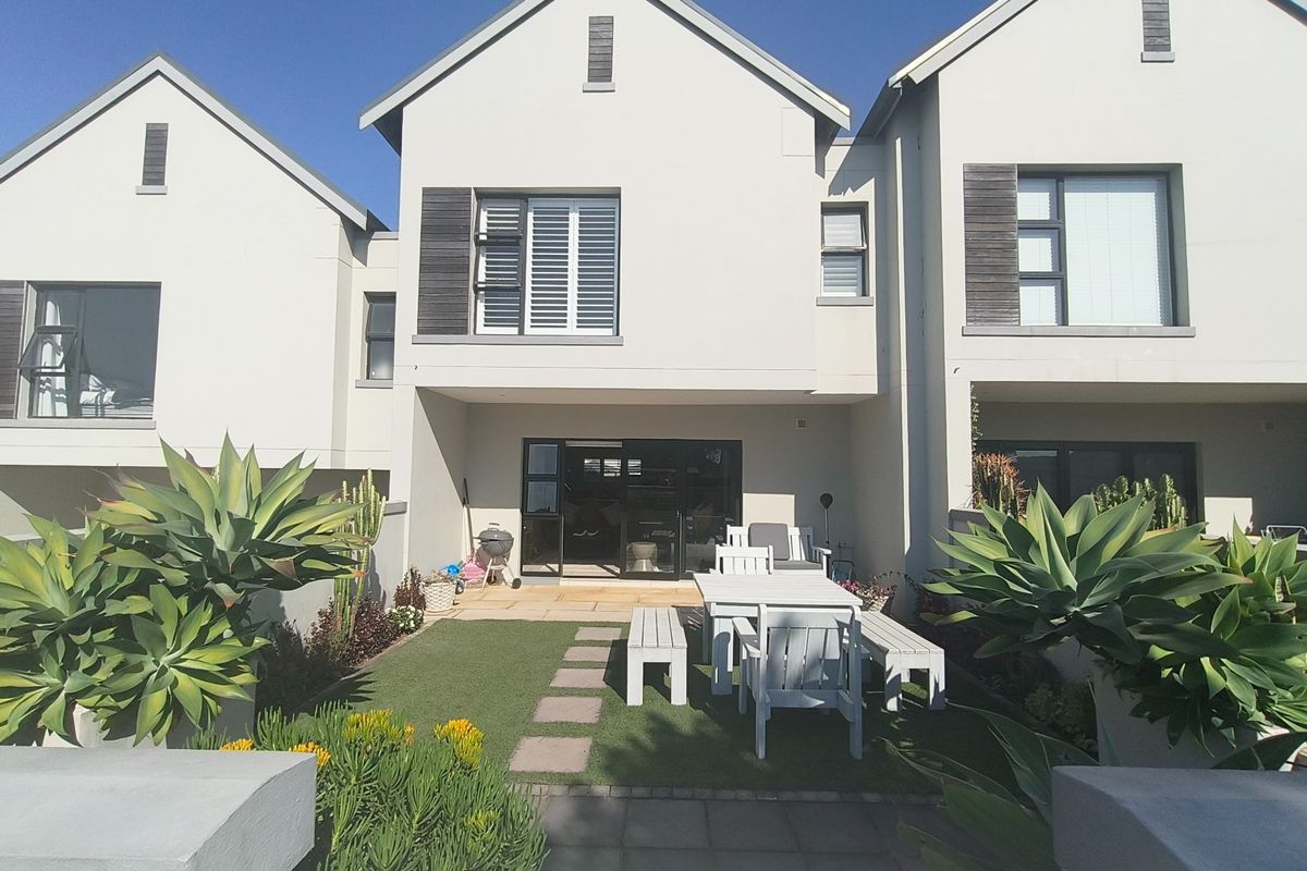 Rear view of a modern townhouse featuring a paved patio, artificial lawn, and sliding glass doors leading into the living area.