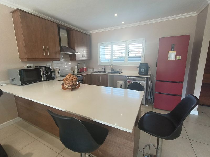 Modern kitchen featuring wood-finish cabinetry, quartz countertops, a breakfast bar, and integrated stainless steel extractor fan with tiled flooring.