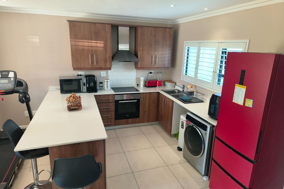 Modern kitchen featuring wood-finish cabinetry, quartz countertops, subway tile backsplash, integrated appliances, and plantation shutters, offering a functional and contemporary cooking space.
