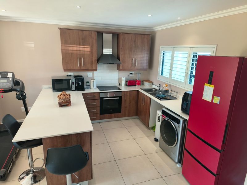 Modern kitchen featuring wood-finish cabinetry, quartz countertops, subway tile backsplash, integrated appliances, and plantation shutters, offering a functional and contemporary cooking space.