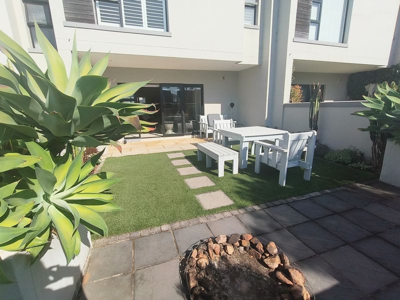 A well-maintained rear courtyard featuring artificial turf, stone paving, a built-in fire pit, and direct access to the home via sliding glass doors.
