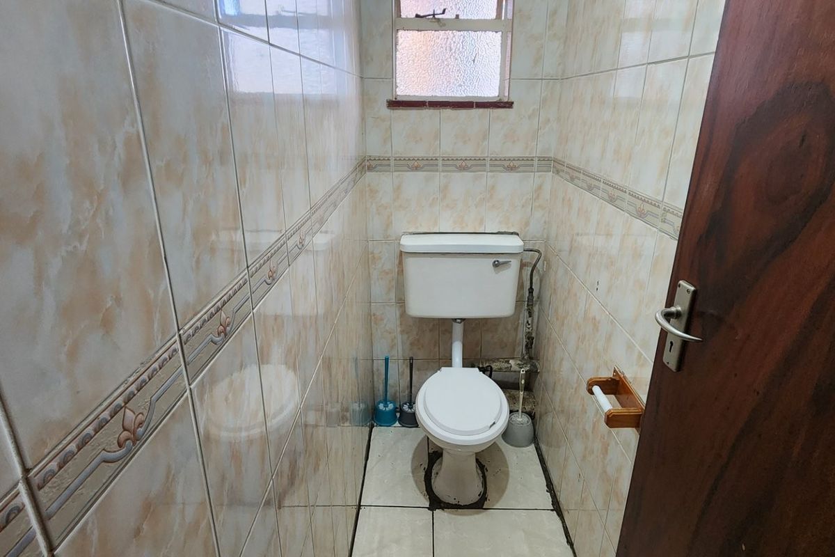 A compact, dated bathroom featuring full-height ceramic wall tiling, a standard toilet, and an obscured glass window for privacy.