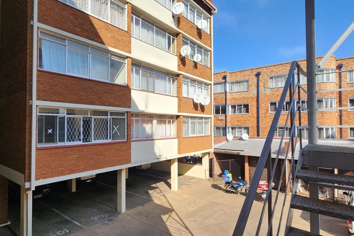 Exterior view of a multi-story brick apartment complex featuring a metal staircase, covered parking bays, and security-fitted windows.