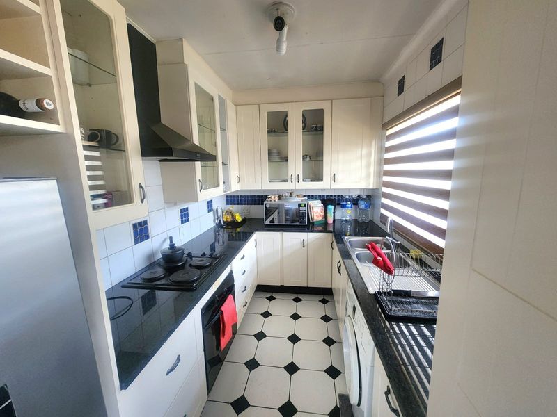 A compact, functional kitchen featuring white cabinetry, black granite countertops, a built-in hob and oven, and classic black and white tiled flooring.