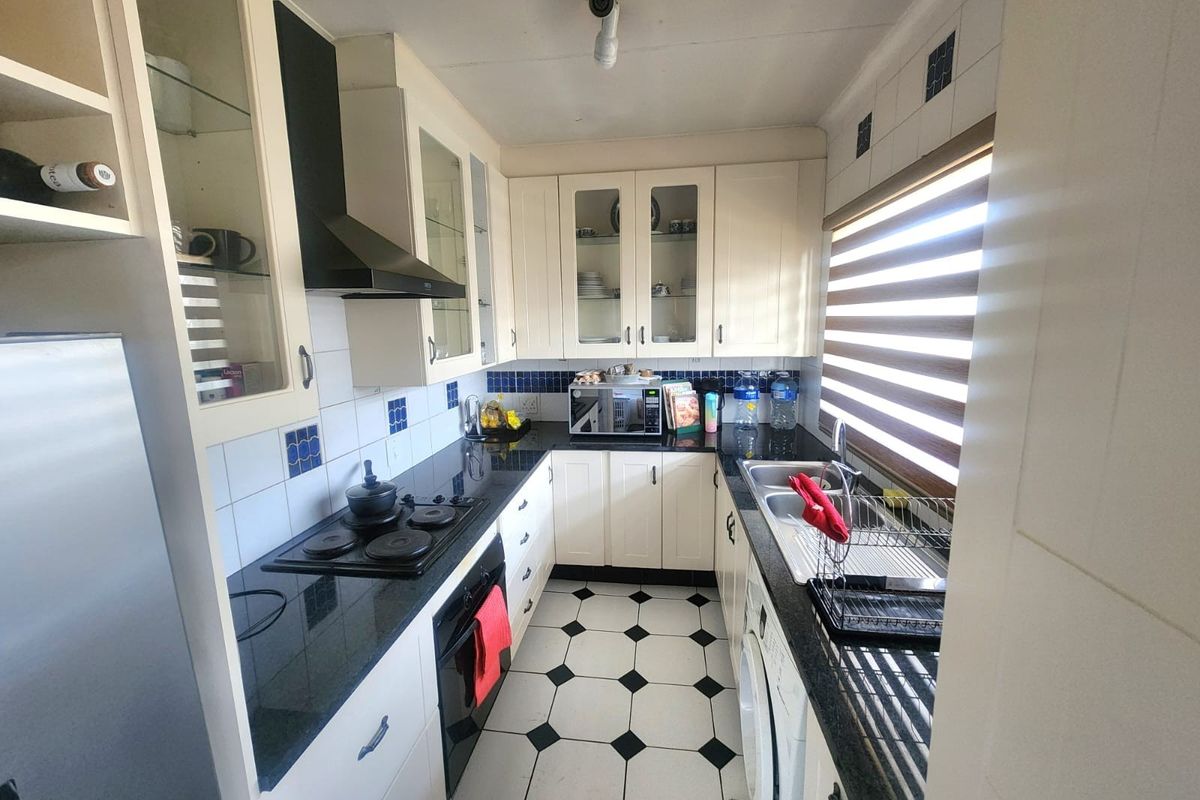A compact, functional kitchen featuring white cabinetry, black granite countertops, a built-in hob and oven, and classic black and white tiled flooring.