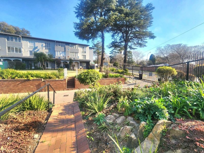 Exterior view of the apartment complex featuring landscaped gardens, brick retaining walls, paved walkways, and secure metal perimeter fencing.
