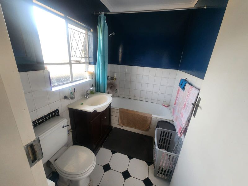 A functional bathroom featuring a bathtub with shower, vanity basin, and toilet, finished with classic black and white floor tiles.