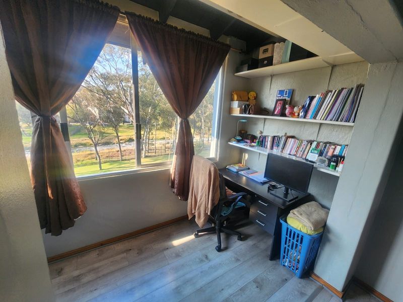 A functional home office space featuring built-in shelving, laminate flooring, and a large window offering pleasant outdoor views.